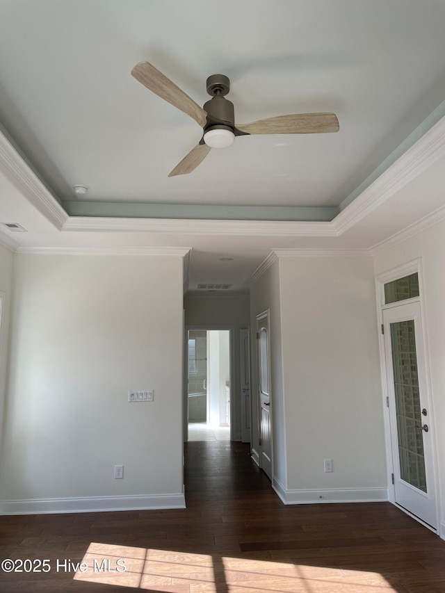 empty room with dark wood finished floors, baseboards, visible vents, ceiling fan, and a raised ceiling