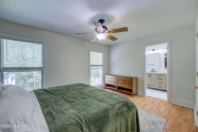 bedroom featuring ceiling fan, ensuite bath, a sink, light wood finished floors, and baseboards