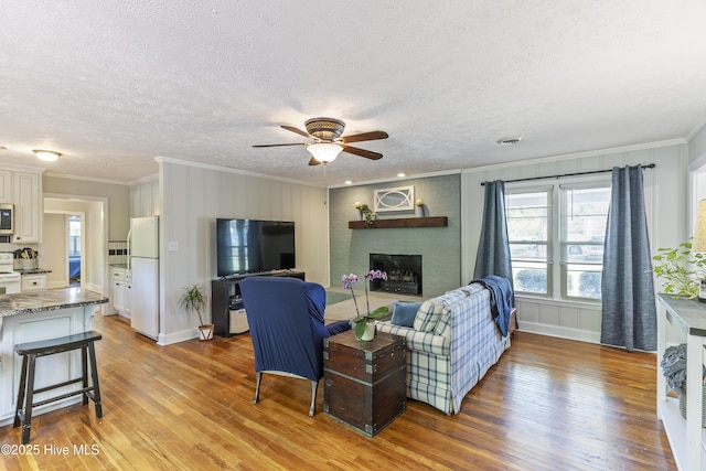 living area with a textured ceiling, light wood-type flooring, a ceiling fan, a brick fireplace, and ornamental molding
