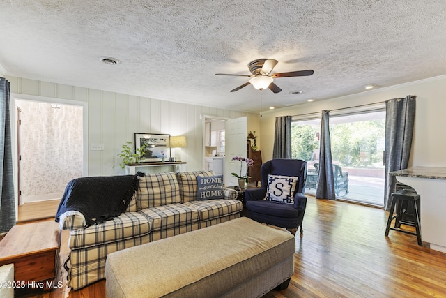 living area featuring a textured ceiling, wood finished floors, visible vents, and ceiling fan