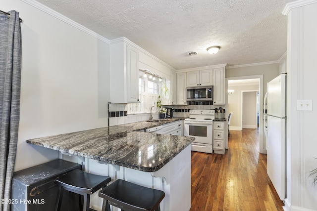 kitchen featuring a sink, a textured ceiling, white appliances, a peninsula, and dark wood-style floors