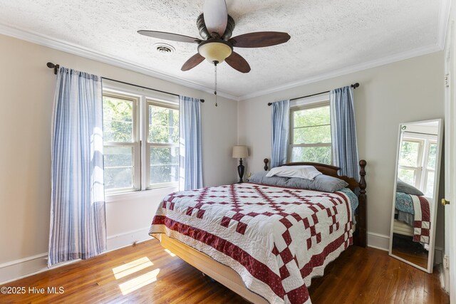 bedroom with crown molding, wood finished floors, a textured ceiling, baseboards, and visible vents