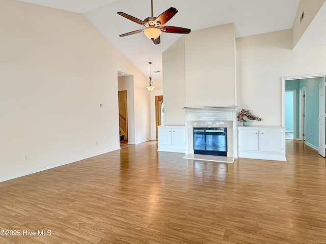 unfurnished living room with high vaulted ceiling, a ceiling fan, wood finished floors, a glass covered fireplace, and stairs