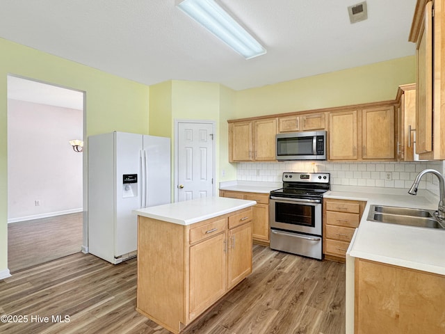 kitchen with appliances with stainless steel finishes, a sink, light wood-type flooring, and decorative backsplash
