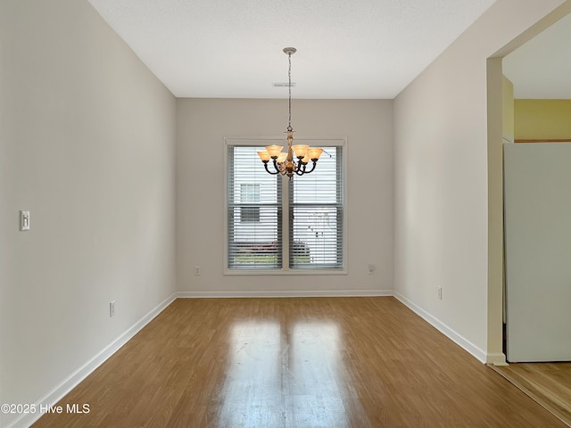 unfurnished dining area with a chandelier, wood finished floors, and baseboards