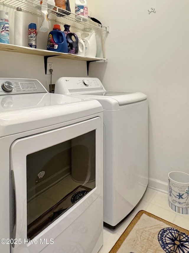clothes washing area with washing machine and dryer, light tile patterned floors, and baseboards