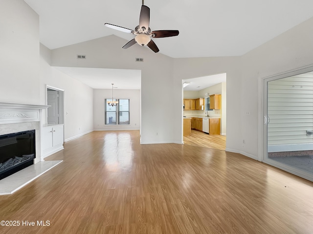 unfurnished living room with ceiling fan, a chandelier, light wood-style floors, a fireplace, and high vaulted ceiling