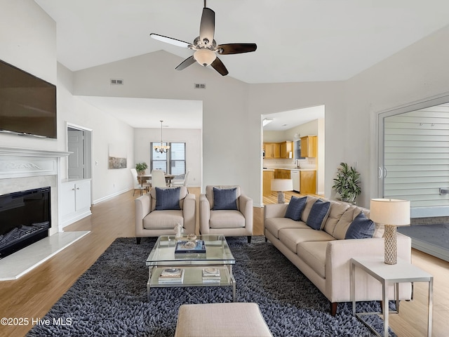 living room with wood finished floors, a ceiling fan, vaulted ceiling, a fireplace, and a chandelier