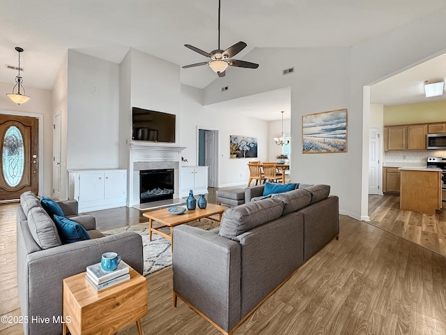 living room featuring high vaulted ceiling, wood finished floors, a ceiling fan, a premium fireplace, and baseboards