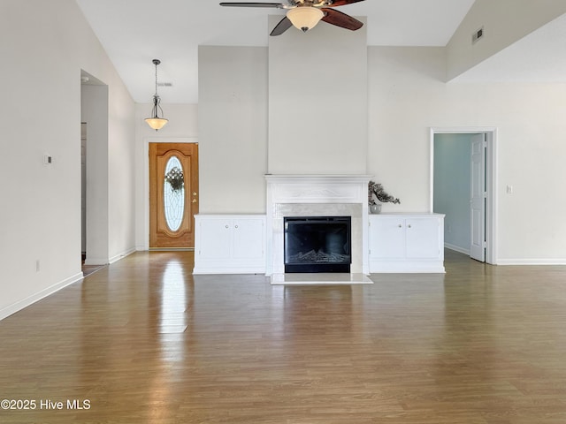 unfurnished living room with a ceiling fan, wood finished floors, a premium fireplace, high vaulted ceiling, and baseboards
