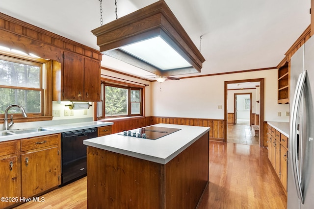 kitchen featuring wainscoting, a sink, light wood finished floors, light countertops, and black appliances