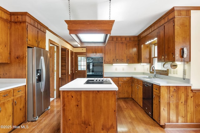 kitchen with brown cabinetry, a kitchen island, a sink, light wood-style flooring, and black appliances