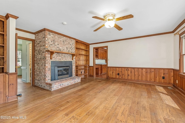 unfurnished living room featuring light wood-style floors, a ceiling fan, built in features, and a wainscoted wall