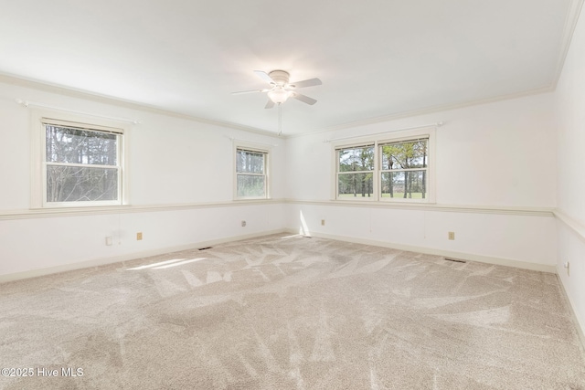 carpeted empty room featuring baseboards, ornamental molding, ceiling fan, and visible vents