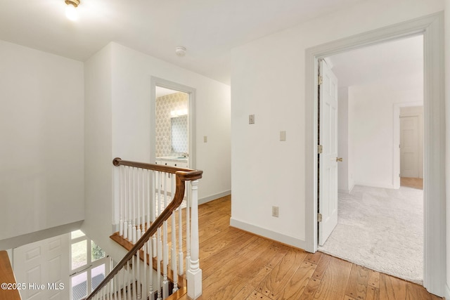 hall with baseboards, light wood-style flooring, and an upstairs landing
