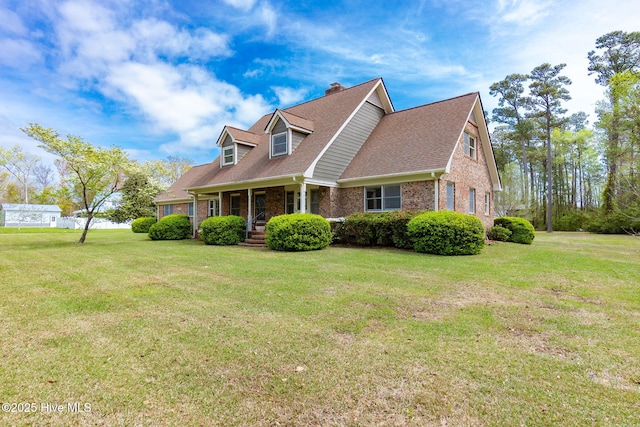 cape cod home featuring brick siding, a front yard, covered porch, and a chimney