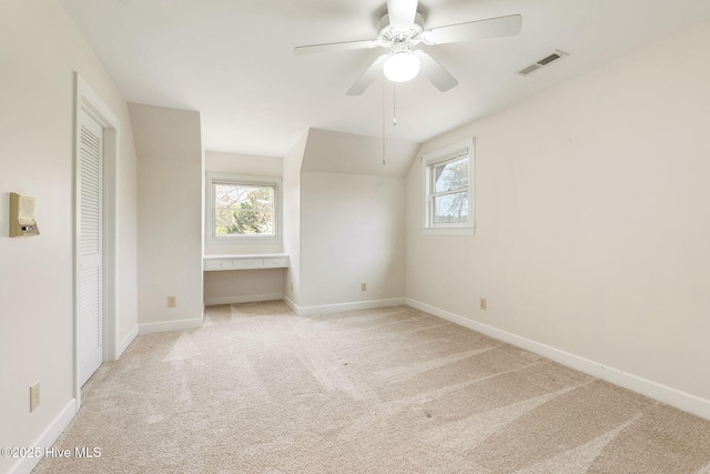 unfurnished bedroom with ceiling fan, visible vents, light colored carpet, baseboards, and lofted ceiling