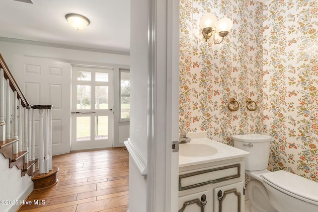 bathroom with wood-type flooring, crown molding, vanity, toilet, and wallpapered walls