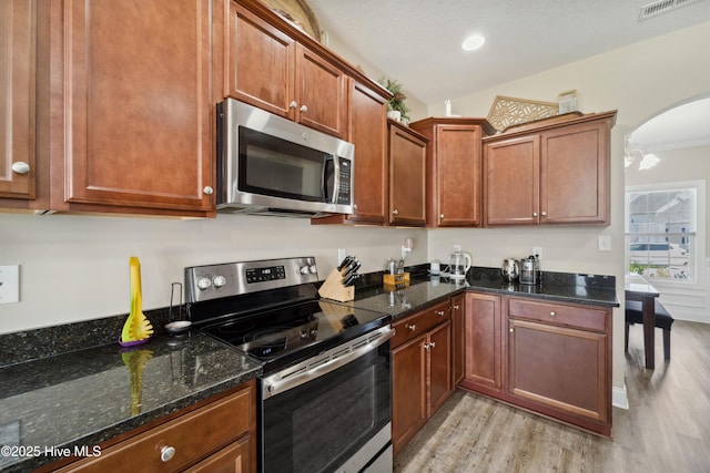 313 March Sea Ln, Jacksonville, NC 28546 - kitchen with stainless steel appliances, light wood finished floors, arched walkways, dark stone countertops, and brown cabinets