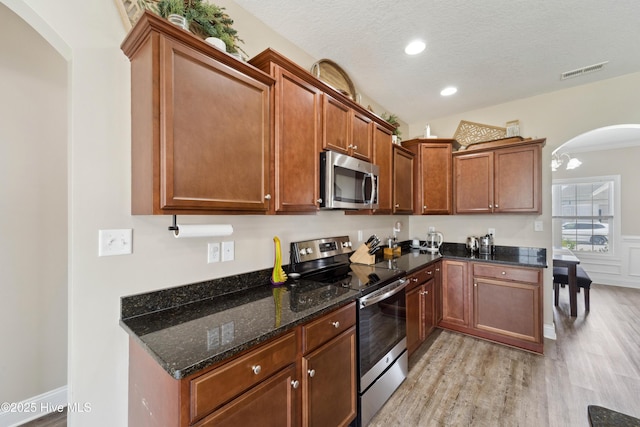 313 March Sea Ln, Jacksonville, NC 28546 - kitchen featuring stainless steel appliances, arched walkways, light wood-type flooring, dark stone counters, and a textured ceiling