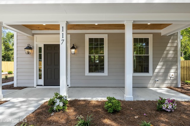 doorway to property with a porch and fence