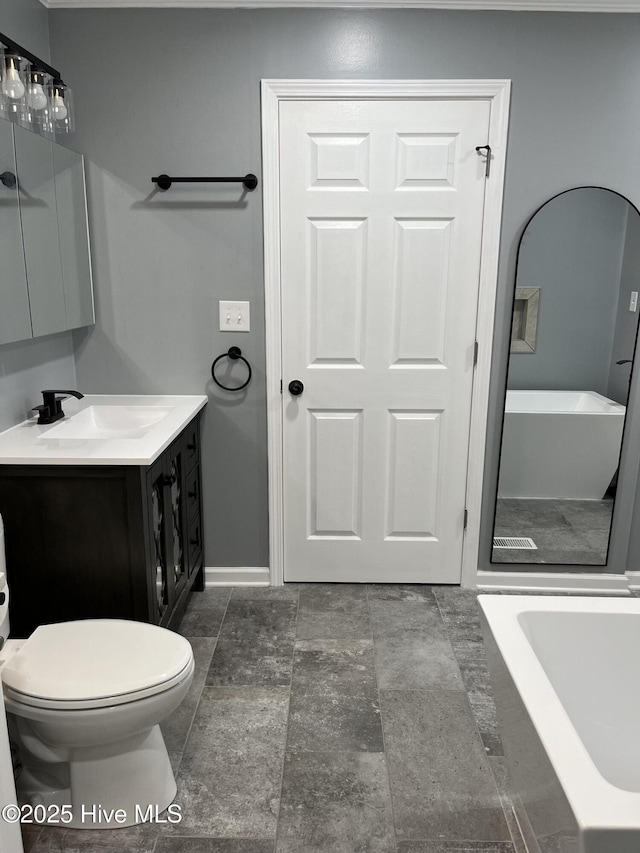 full bath with vanity, toilet, stone finish floor, a tub, and baseboards