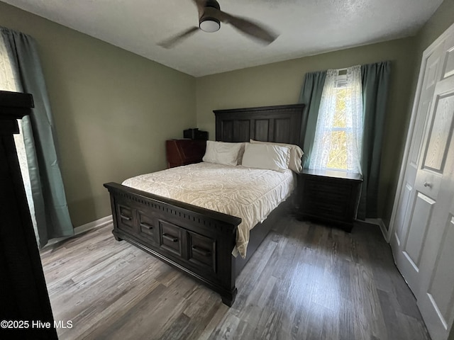 bedroom featuring a ceiling fan, baseboards, dark wood-style floors, and a closet