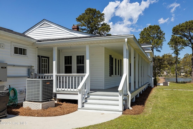view of front facade featuring a front lawn, covered porch, central air condition unit, and a chimney