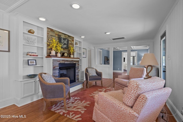 living room featuring a fireplace, wood finished floors, built in shelves, and ornamental molding