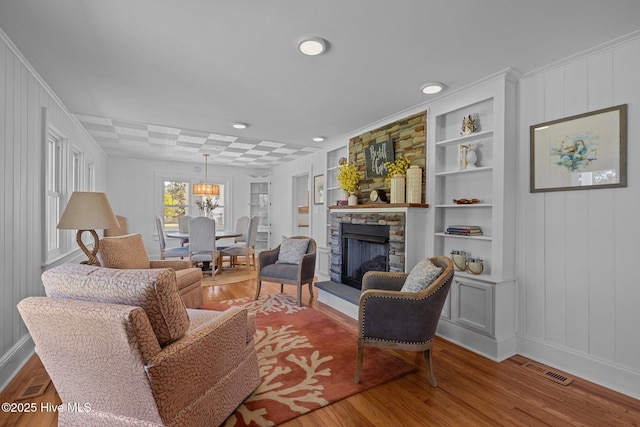 living area with a stone fireplace, wood finished floors, a decorative wall, baseboards, and built in shelves
