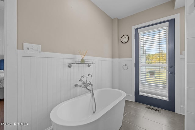 bathroom with wainscoting, tile patterned floors, a freestanding tub, and visible vents