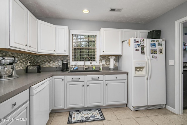 kitchen with white appliances, tasteful backsplash, white cabinetry, a sink, and dark countertops