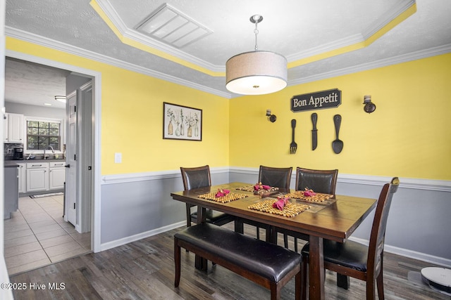 dining room featuring baseboards, ornamental molding, a textured ceiling, a tray ceiling, and wood finished floors