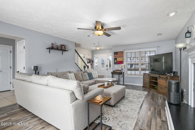 living area featuring wood finished floors, baseboards, a ceiling fan, and stairway