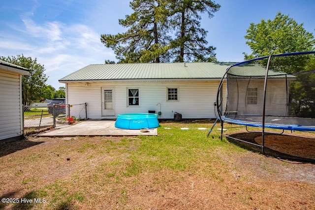 rear view of property featuring metal roof, a trampoline, a lawn, fence, and a patio