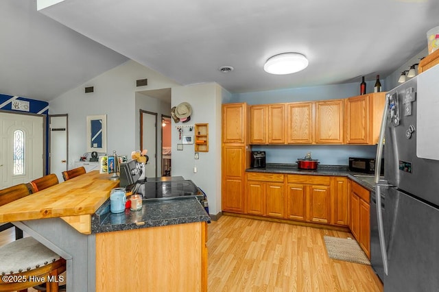 kitchen featuring a breakfast bar area, visible vents, black appliances, and light wood-style floors