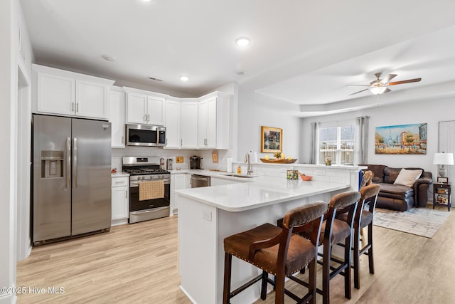 kitchen featuring stainless steel appliances, a peninsula, light wood-style flooring, and a sink