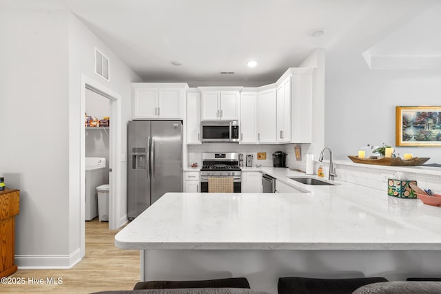 kitchen with a peninsula, light stone countertops, visible vents, stainless steel appliances, and a sink