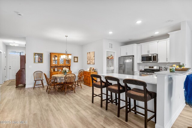 kitchen featuring a kitchen bar, light wood-type flooring, light countertops, stainless steel appliances, and backsplash