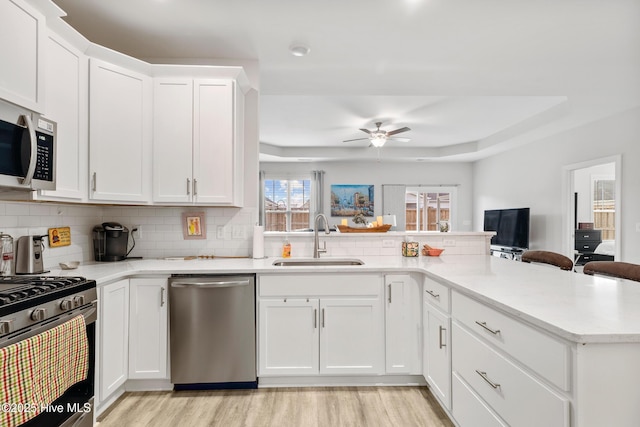 kitchen featuring light wood-style floors, ceiling fan, a peninsula, appliances with stainless steel finishes, and a sink