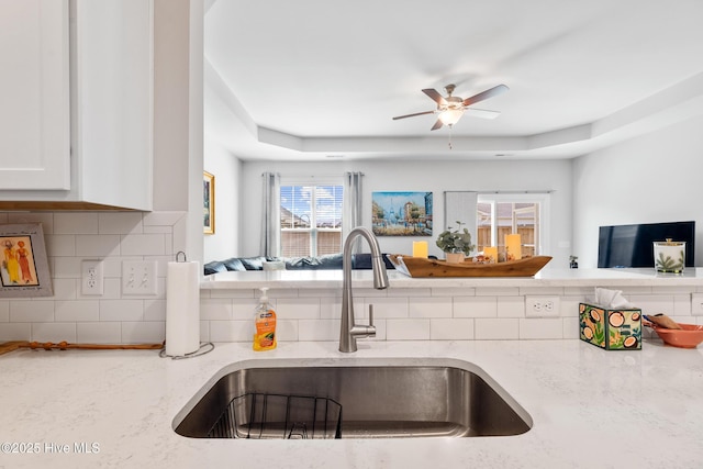kitchen featuring open floor plan, a sink, backsplash, and light stone countertops