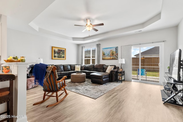 living room with a wealth of natural light, wood finished floors, a ceiling fan, and a raised ceiling