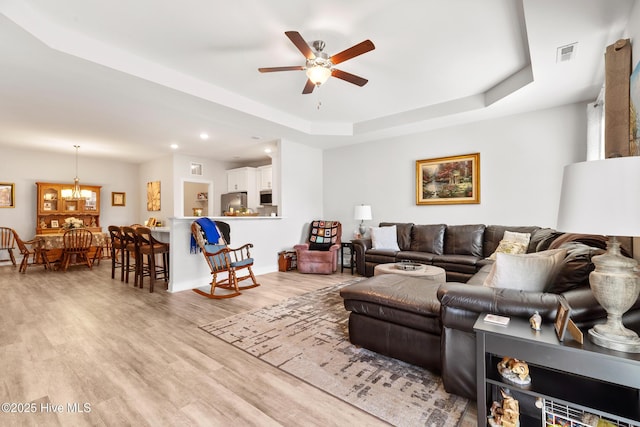 living area featuring recessed lighting, light wood-style floors, visible vents, a tray ceiling, and ceiling fan with notable chandelier