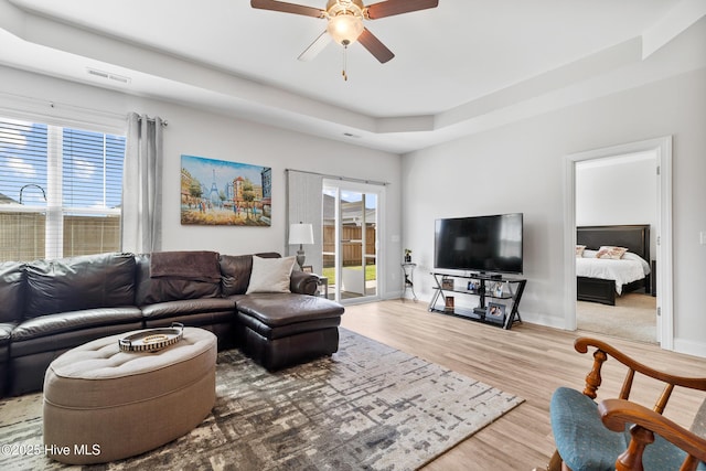 living area with ceiling fan, a tray ceiling, visible vents, wood finished floors, and baseboards