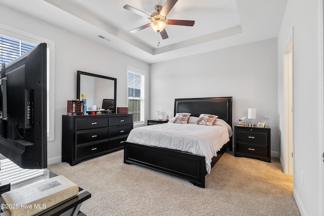 bedroom with a tray ceiling, baseboards, light colored carpet, and visible vents