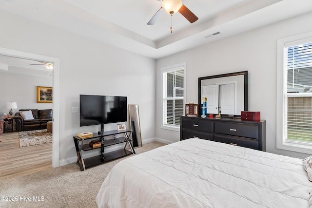 bedroom with visible vents, baseboards, a raised ceiling, and light colored carpet