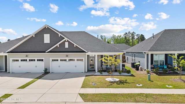 view of front facade featuring roof with shingles, driveway, a front yard, central AC unit, and a garage
