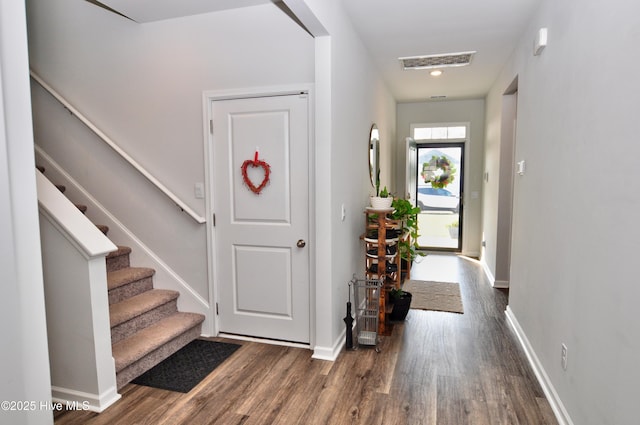 foyer entrance featuring baseboards, visible vents, wood finished floors, and stairway