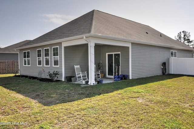 rear view of property with a shingled roof, fence, and a yard