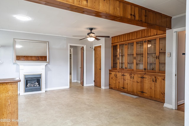 unfurnished living room featuring crown molding, baseboards, ceiling fan, light floors, and a glass covered fireplace